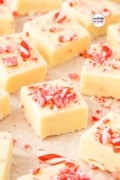 parchment paper on the counter with squares of the fudge just after dusting with candy cane pieces.