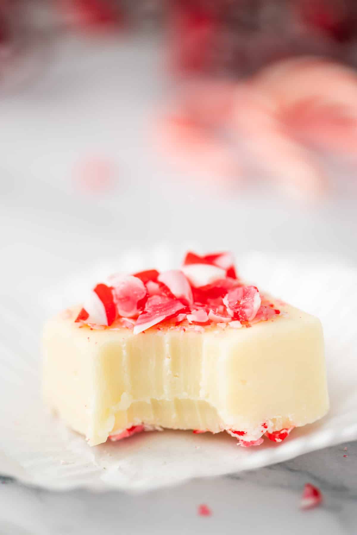 A piece of sweetened condensed milk peppermint fudge with a bite taken out of it set on a open cupcake paper.