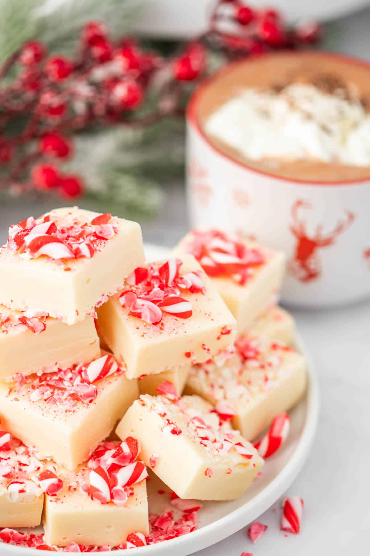 A plate of peppermint fudge pieces with hot cocoa and Christmas decor in the background.