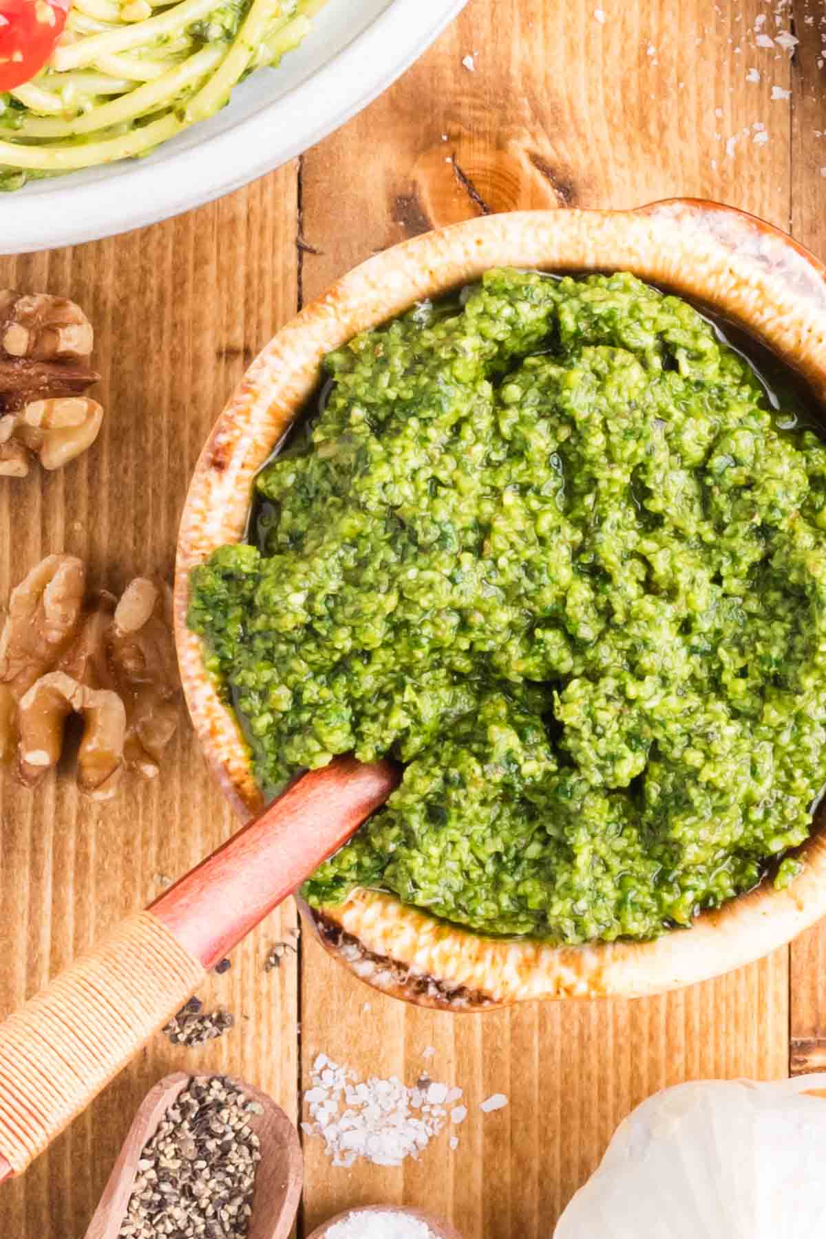 Blassic basil pesto in a bowl with a wooden spoon set on a wooden table.