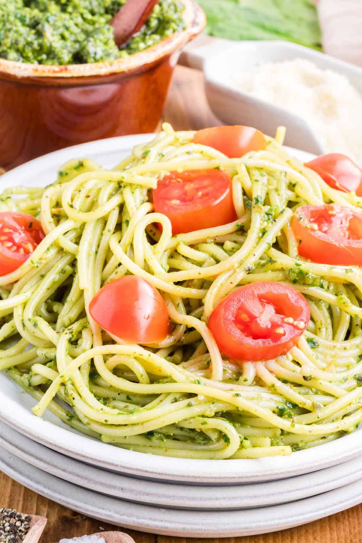 A white plate a pesto pasta with cherry tomatoes.