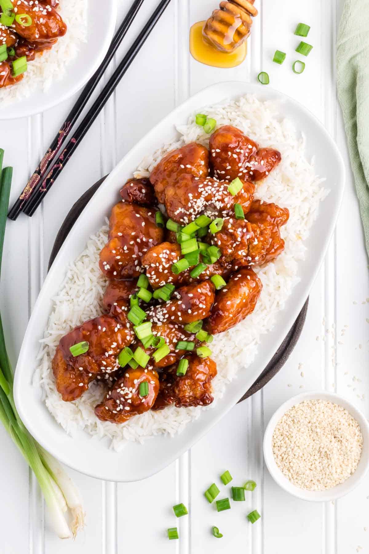 An oblong white serving platter with rice and sesame chicken.