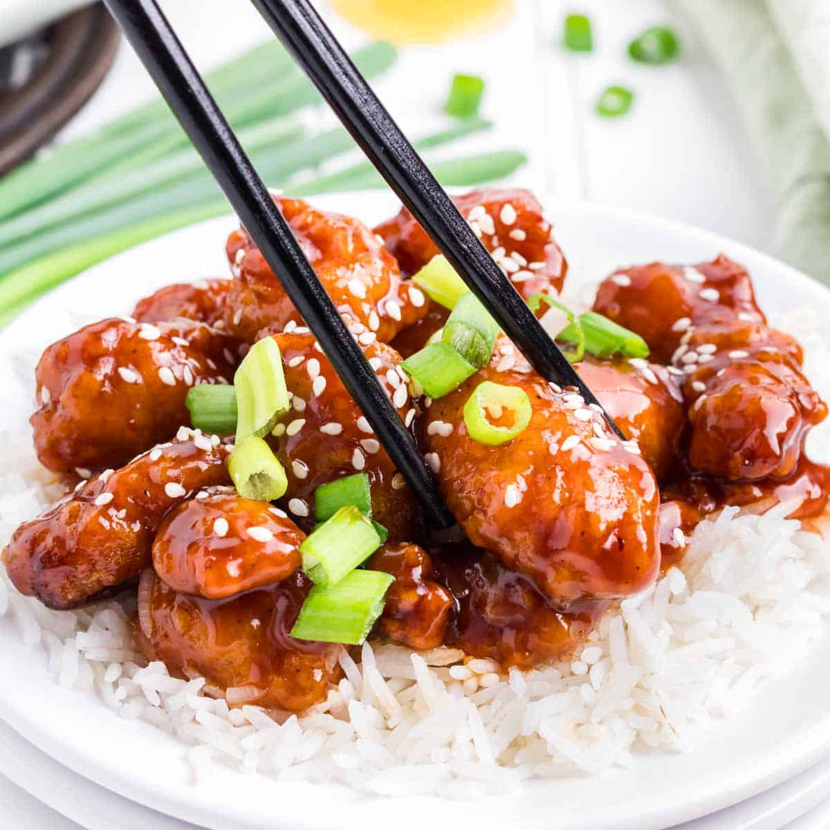 Black chopsticks picking up a piece of sesame chicken.