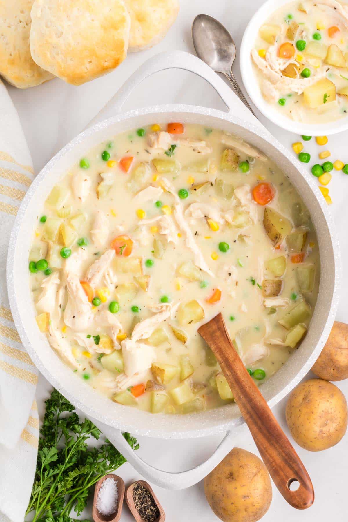 A soup pot filled with chicken pot pie soup being stirred with a wooden spoon.