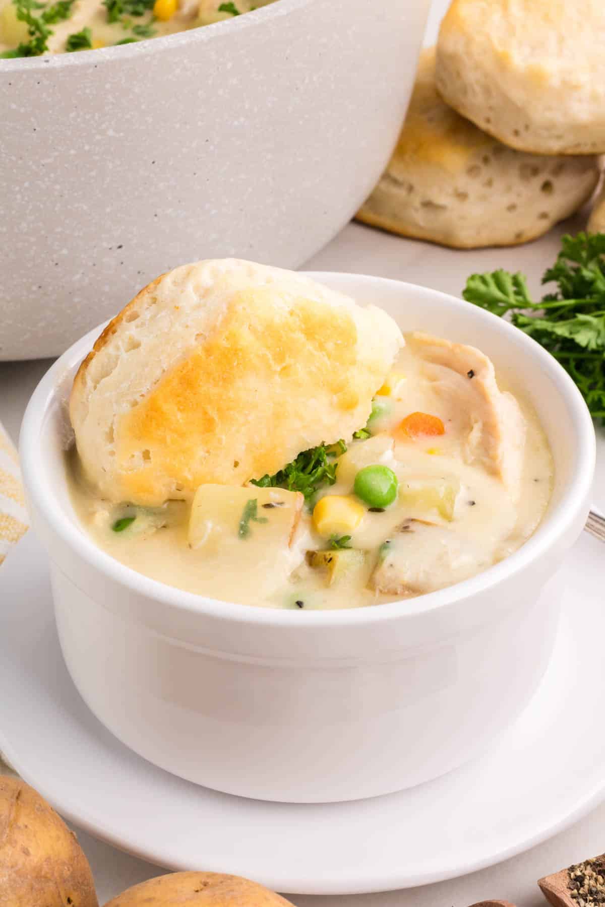 A white cup filled with chicken pot pie soup and topped with a biscuit.