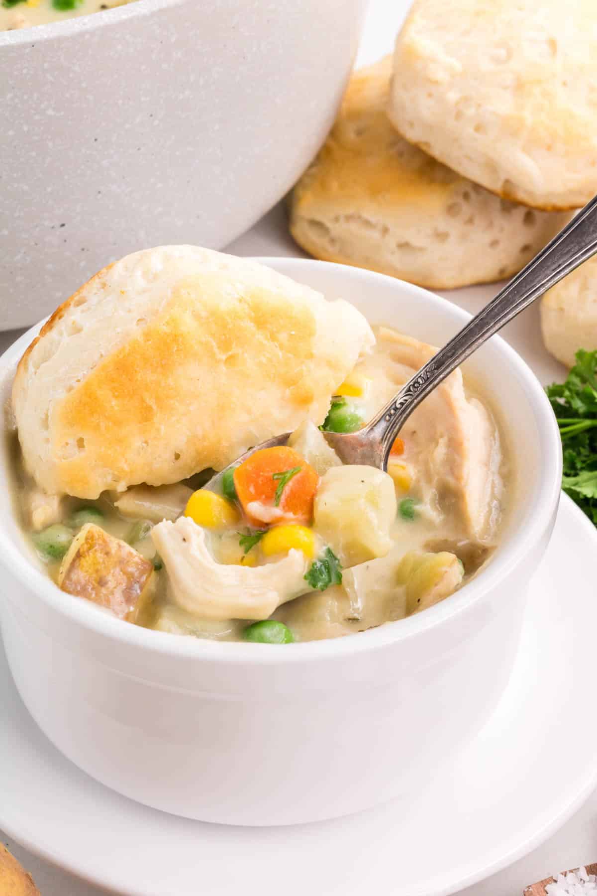 A silver spoon take a bite from a cup of chicken pot pie soup.