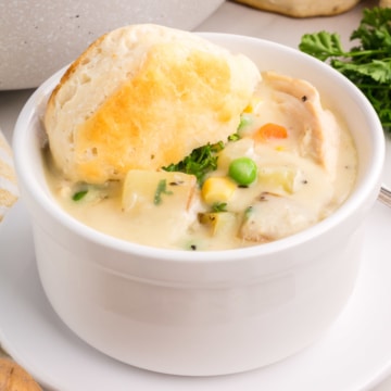 A white cup filled with chicken pot pie soup and topped with a biscuit.