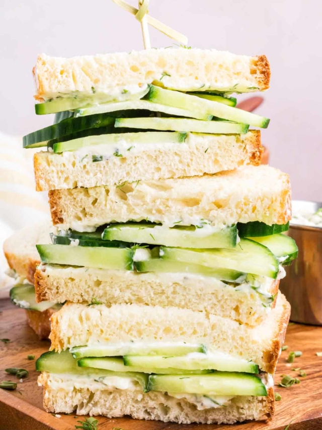 Cucumber sandwiches stacked on top of each other with dill and chives sprinkled for garnish.