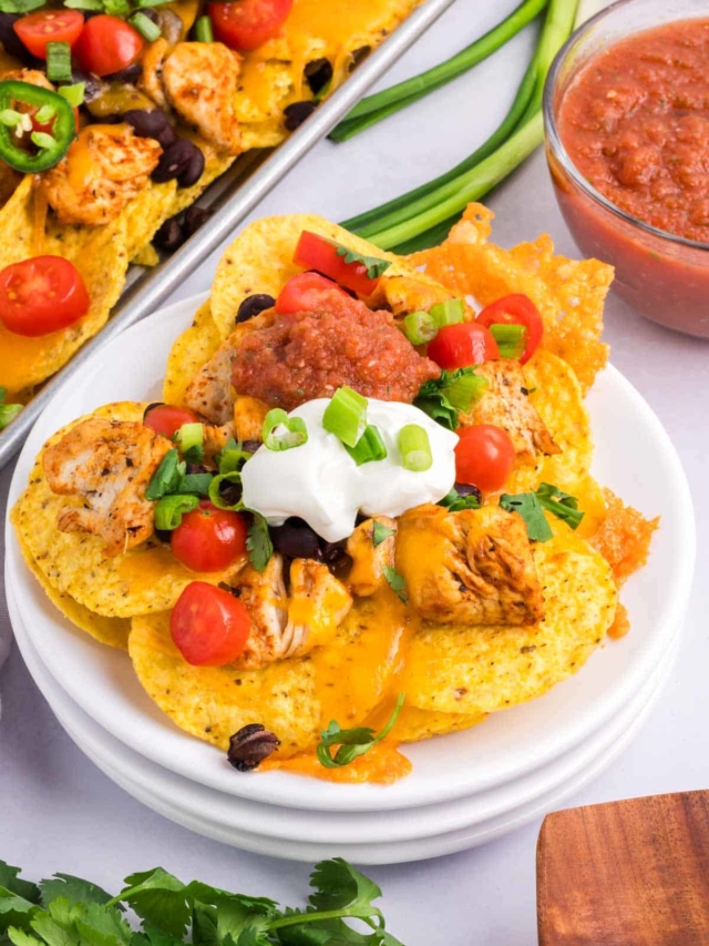 A white plate with a serving of chicken nachos topped with sour cream, salsa and cilantro.