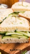 Cucumber sandwiches sliced in half on a wood cutting board.