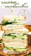 Cucumber sandwich half featured on a wood cuting board and wrapped in brown food safe paper.