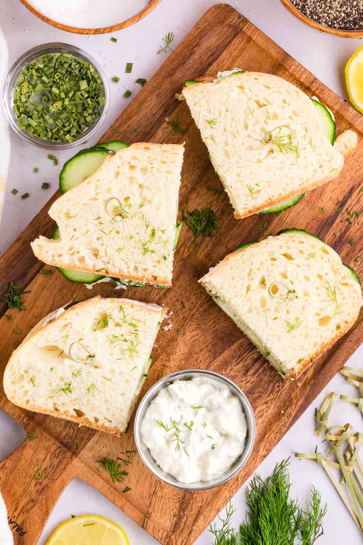 Cucumber sandwiches sliced in half on a wooden cutting board.