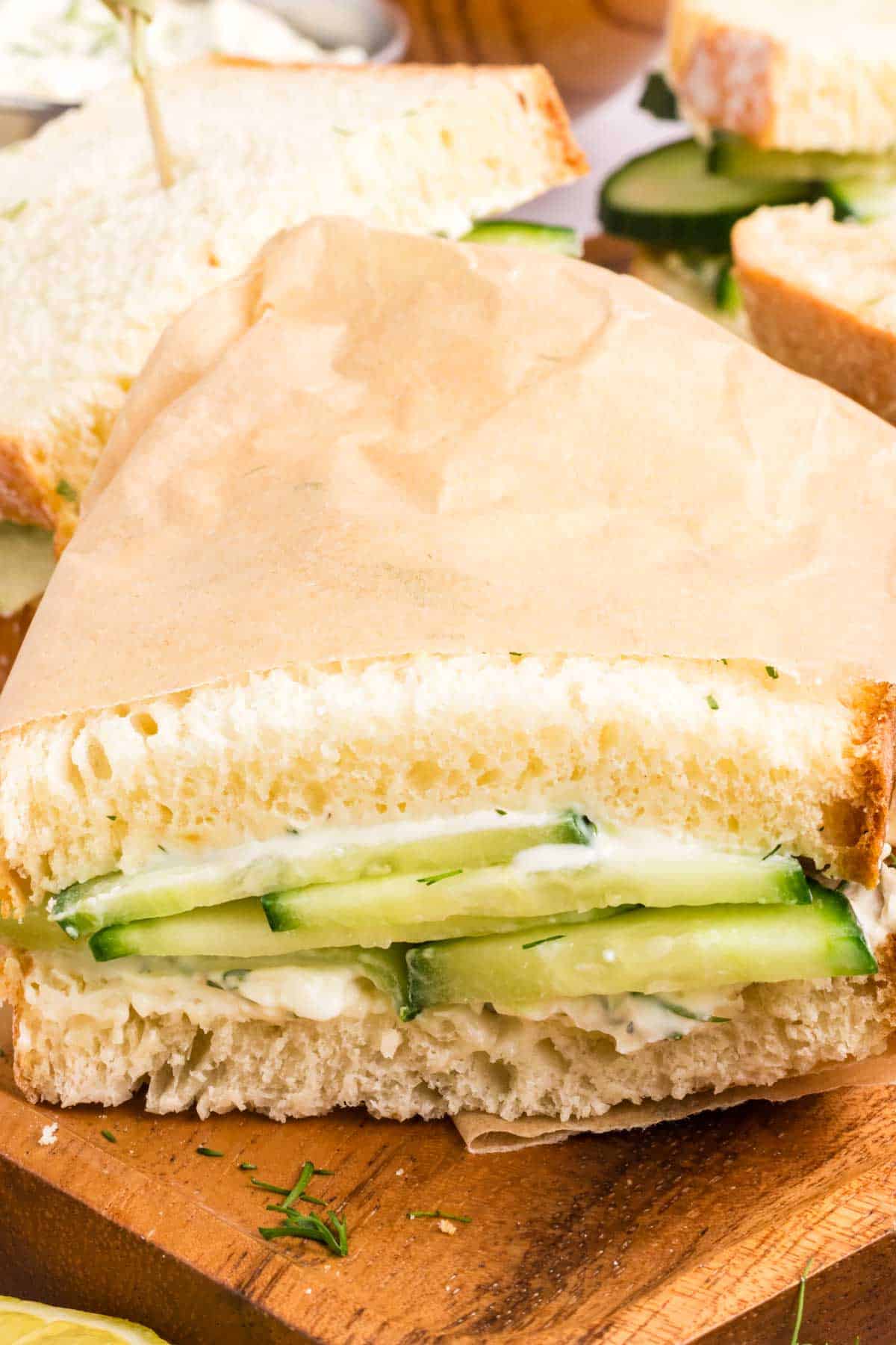 A cucumber sandwich sliced in half and wrapped in brown wax paper.