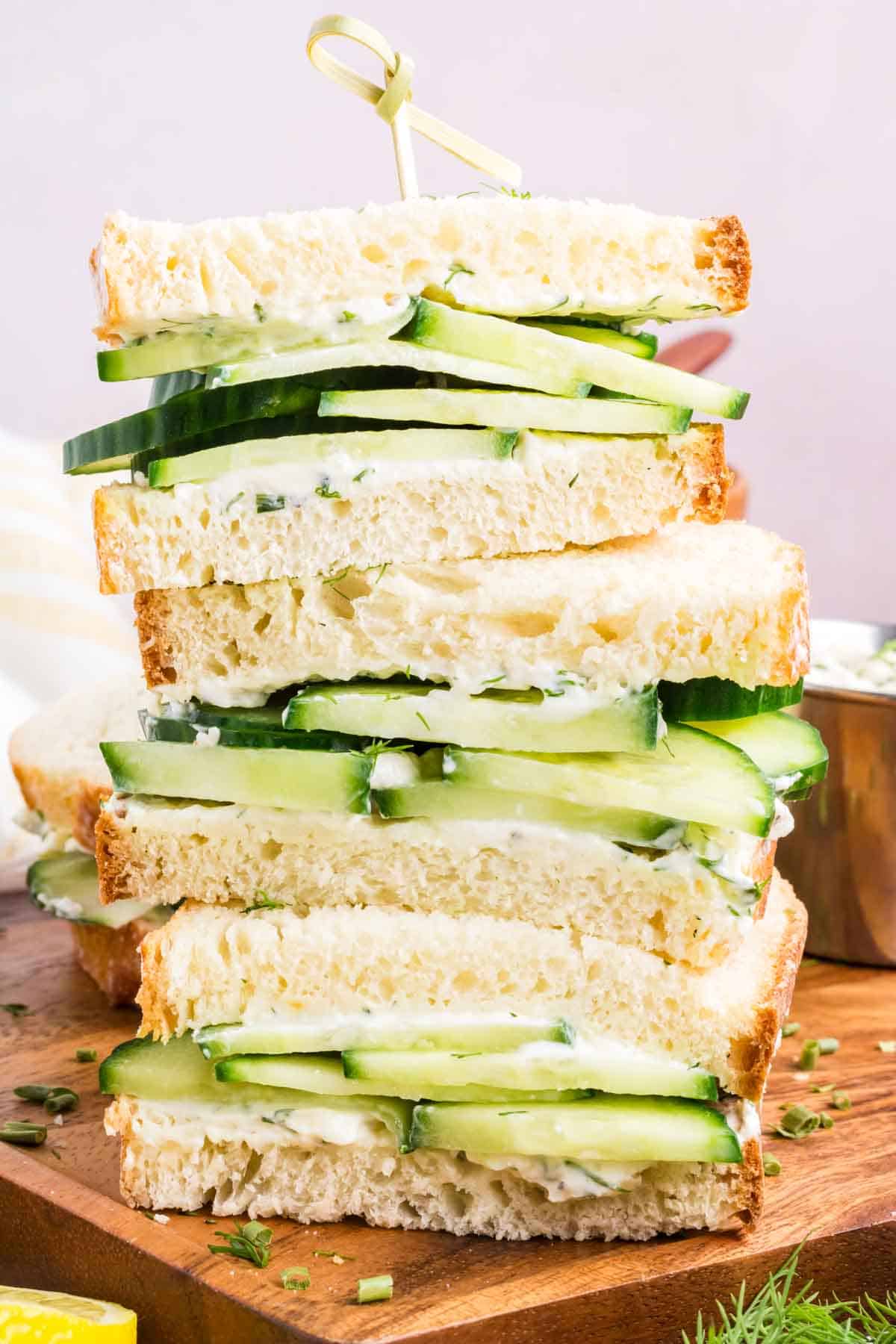 Cucumber sandwiches stacked on top of each other with dill and chives sprinkled for garnish.
