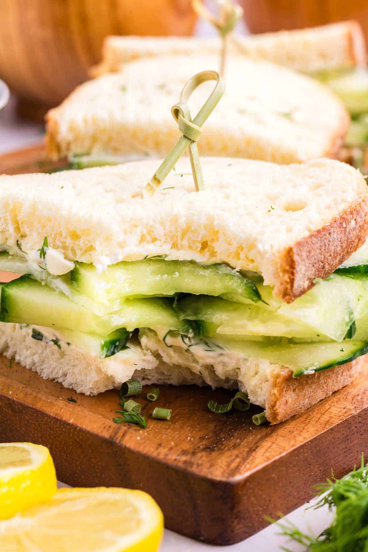 A cucumber sandwich with a bite taken from the sandwich.