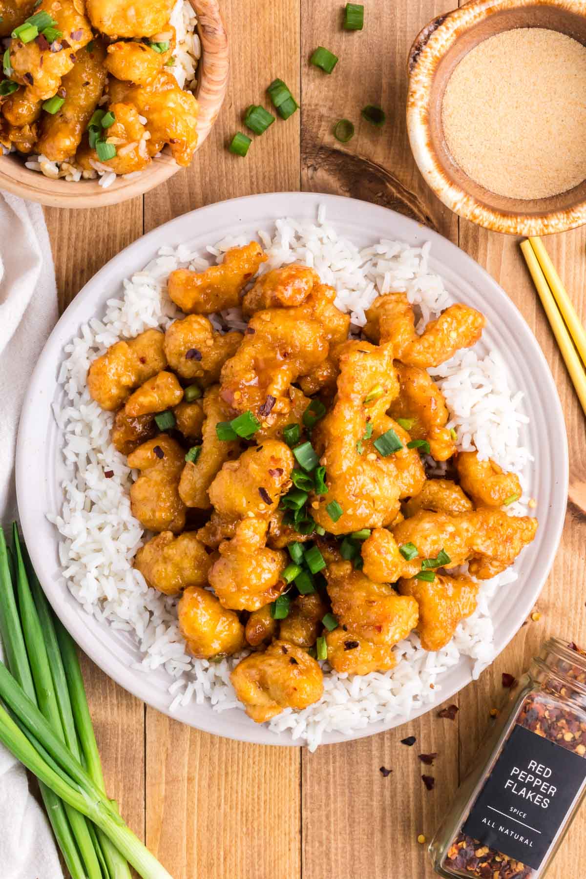 A serving plate with white rice and honey garlic chicken garnished with green onion slices.