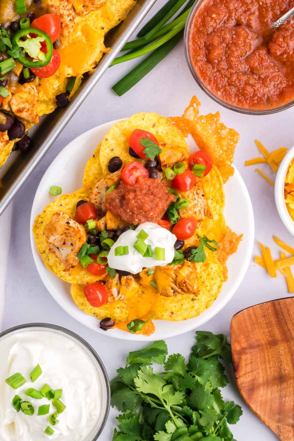 Easy Chicken nachos on a white plate set on a table with toppings around.