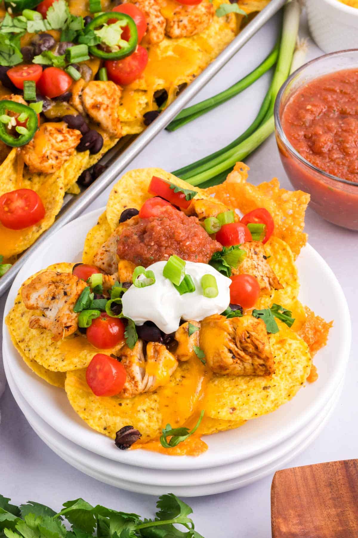 A white plate with a serving of chicken nachos topped with sour cream, salsa and cilantro.