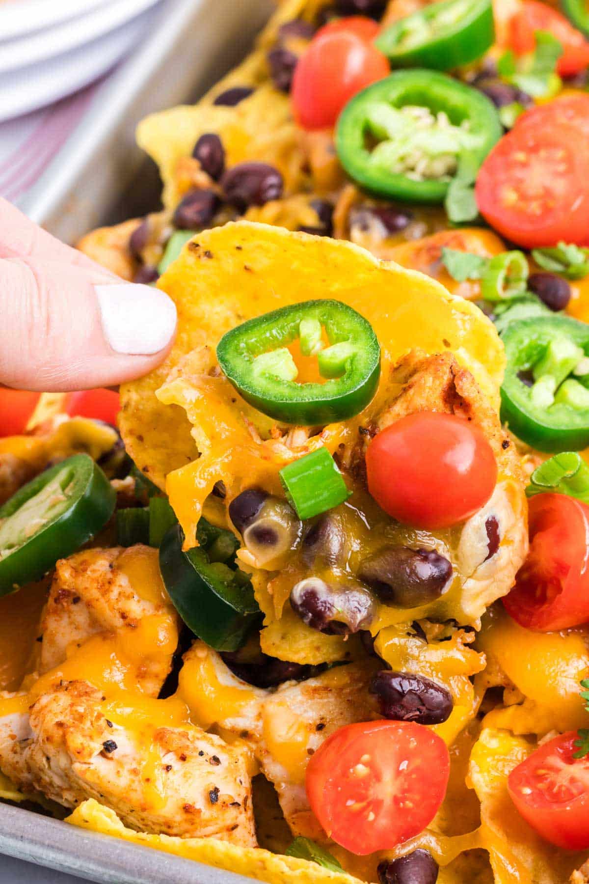 A hand picking up a tortilla chip with nacho toppings.