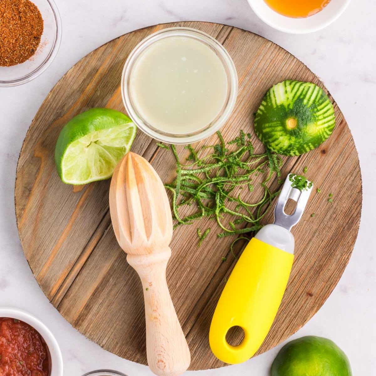 A round cutting board with a zested lime and the juice of a lime.