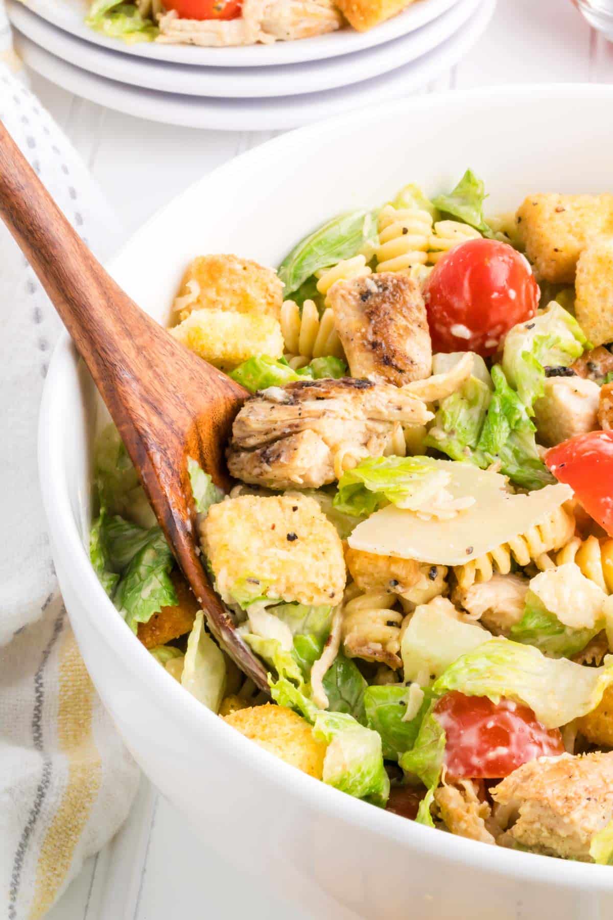 A wooden serving spoon scooping out a serving of Caesar Chicken Pasta Salad.
