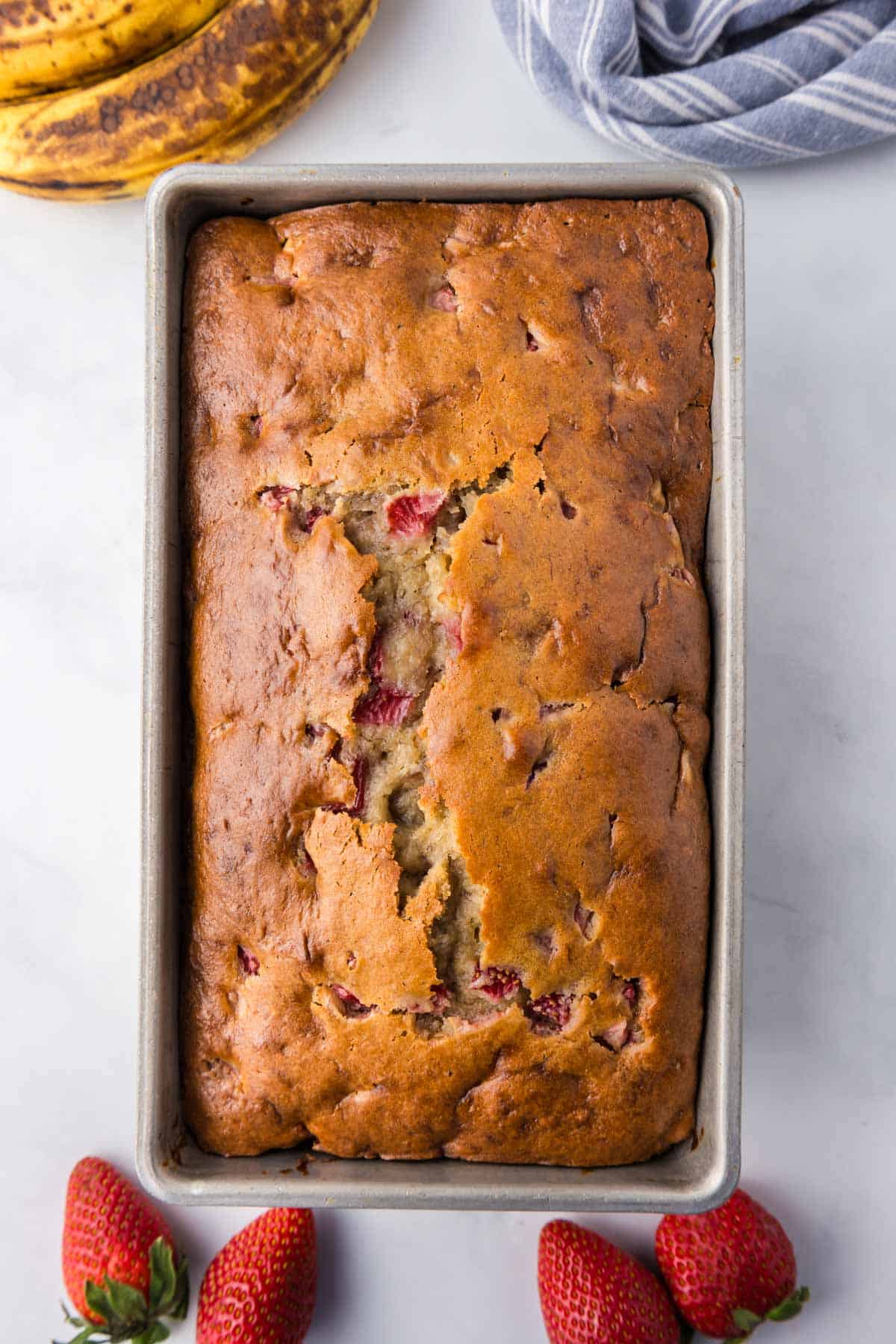 A loaf of strawberry banana bread in a metal loaf pan.