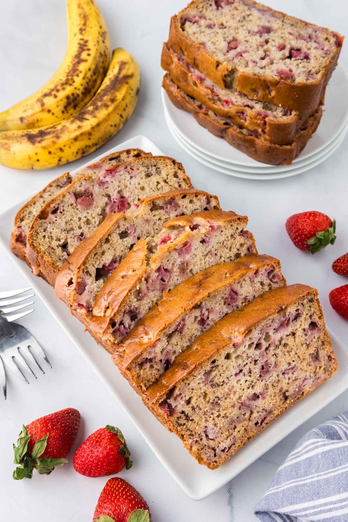 A sliced loaf of strawberry banana bread set on a white table.