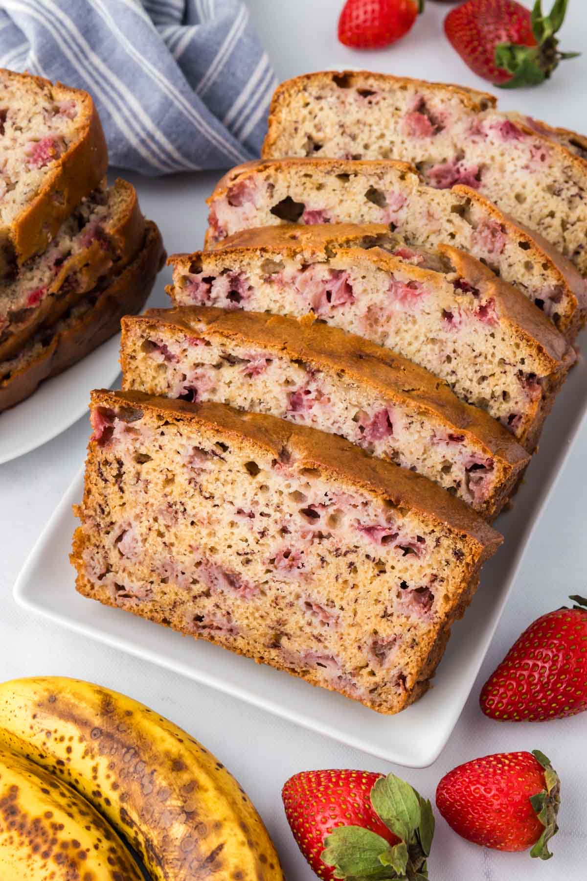 A sliced loaf of strawberry banana bread set on a white table.