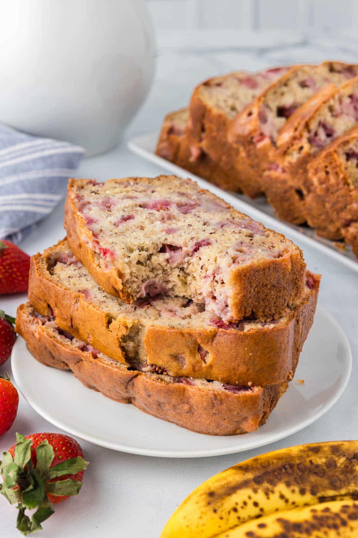 Three slices of strawberry banana bread on a white plate with a bite taken from the top slice.