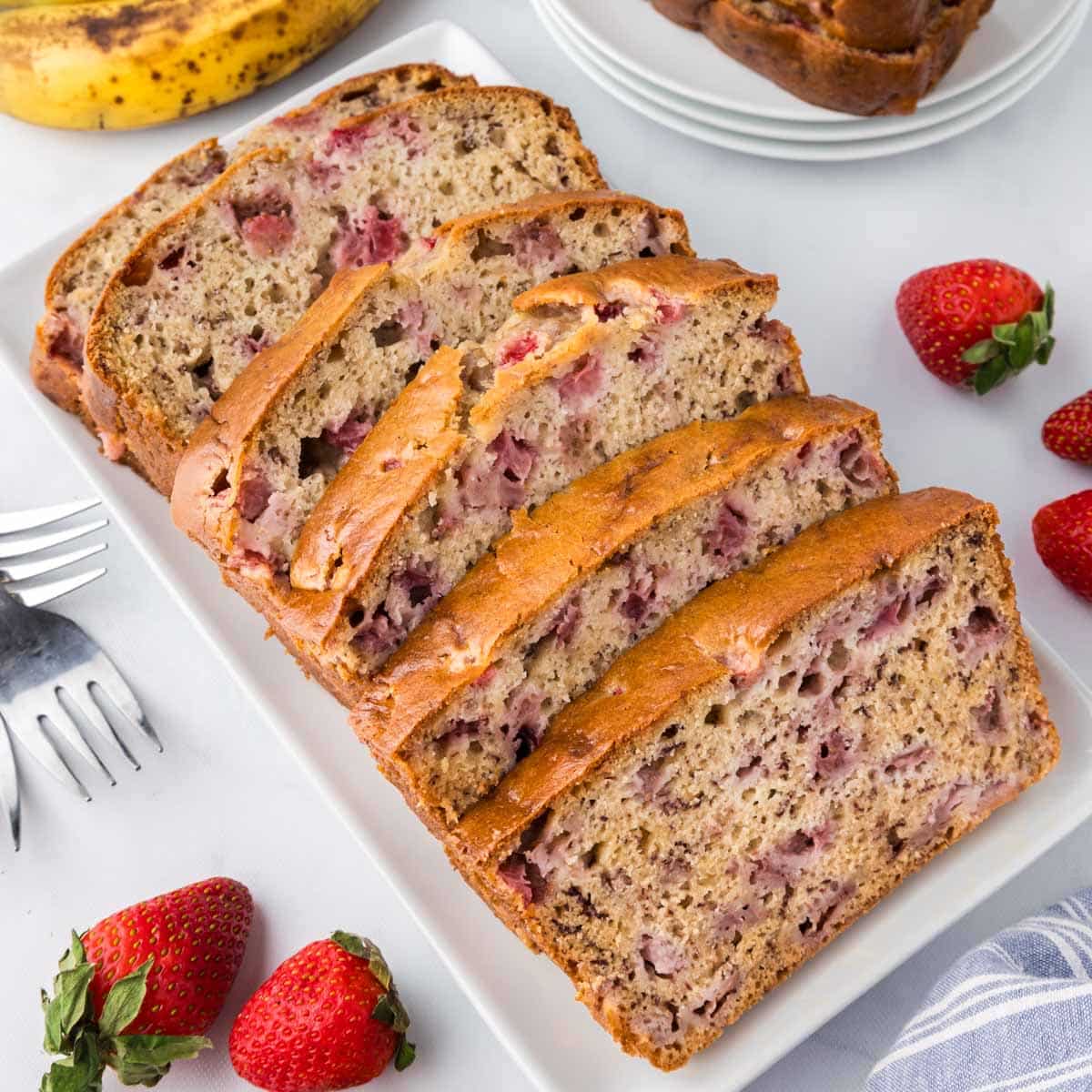 A sliced loaf of strawberry banana bread set on a white table.
