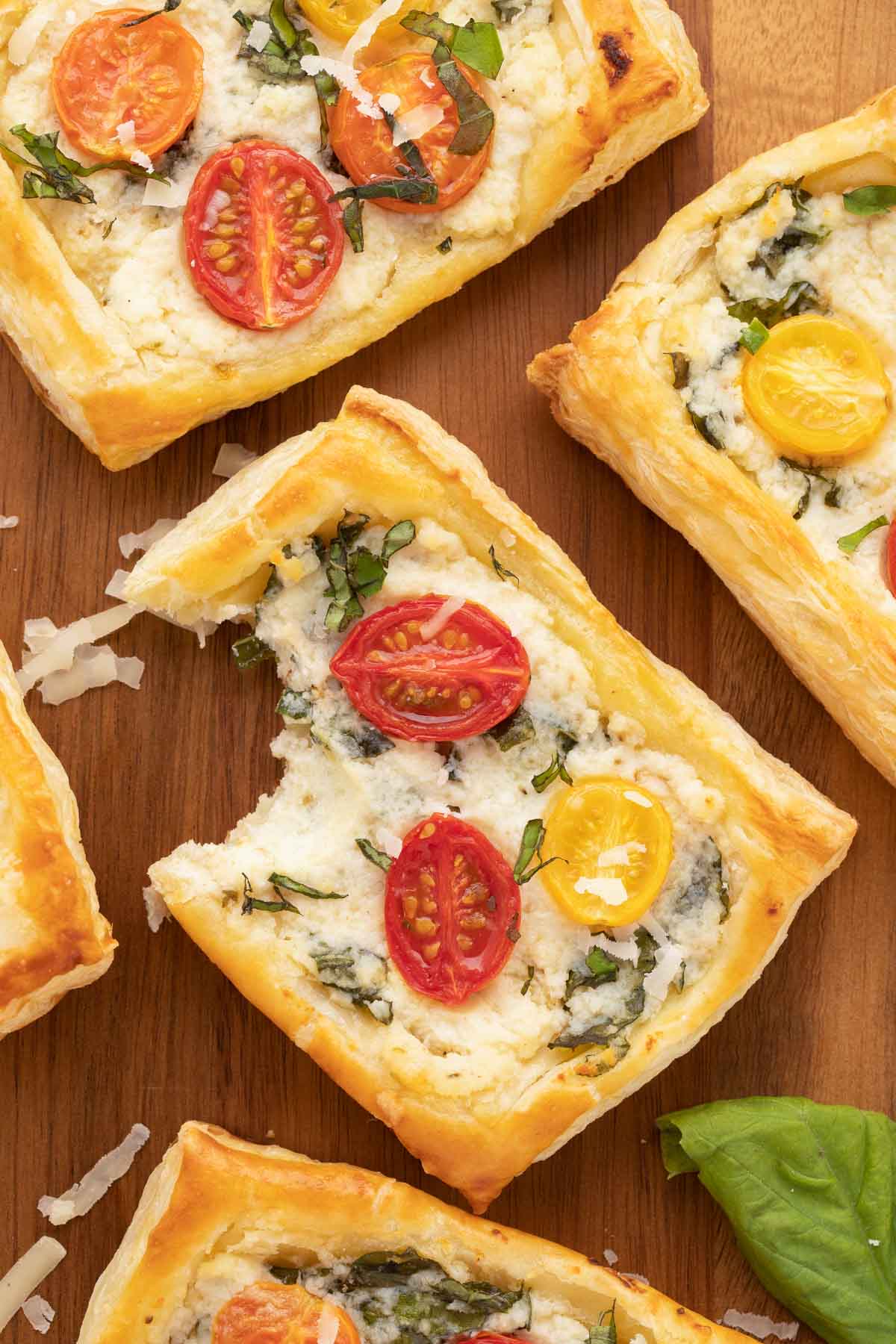 Individual tomato tarts with puff pastry on a wooden serving board.