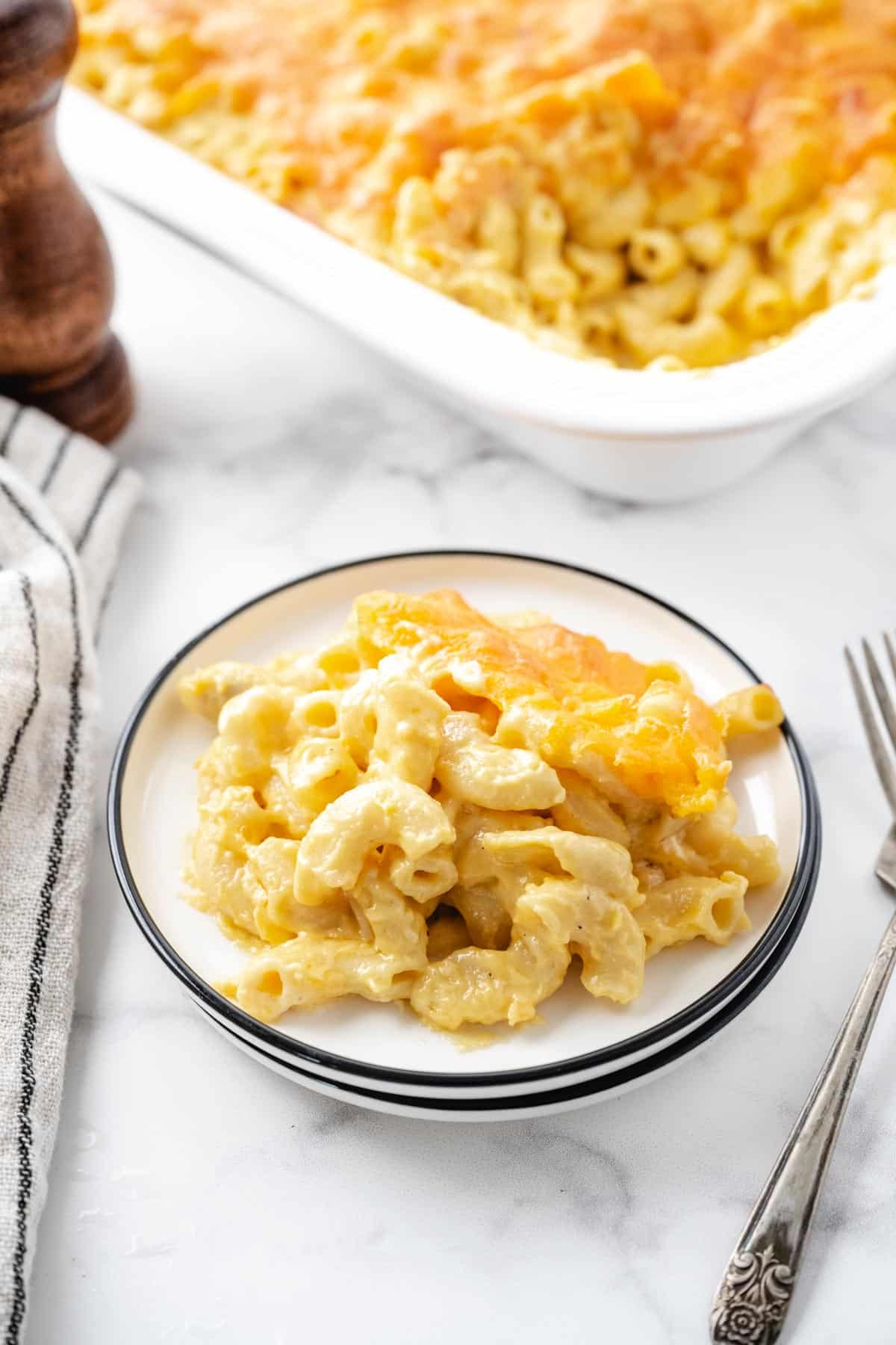 A plate of mac and cheese with the casserole dish set on the table in the background.