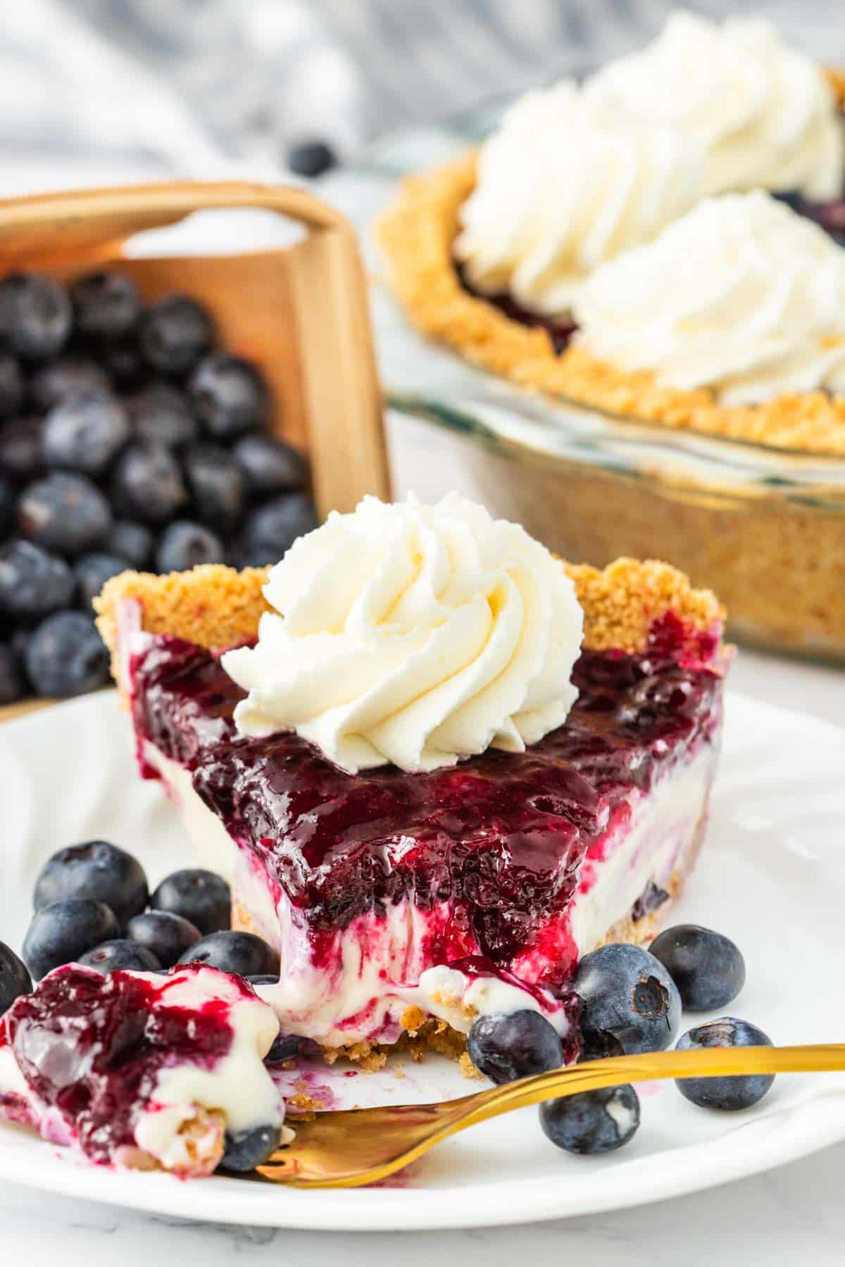 A gold fork removing a bite of blueberry pie.