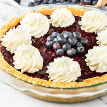A whole blueberry cheesecake pie in a glass pie dish.