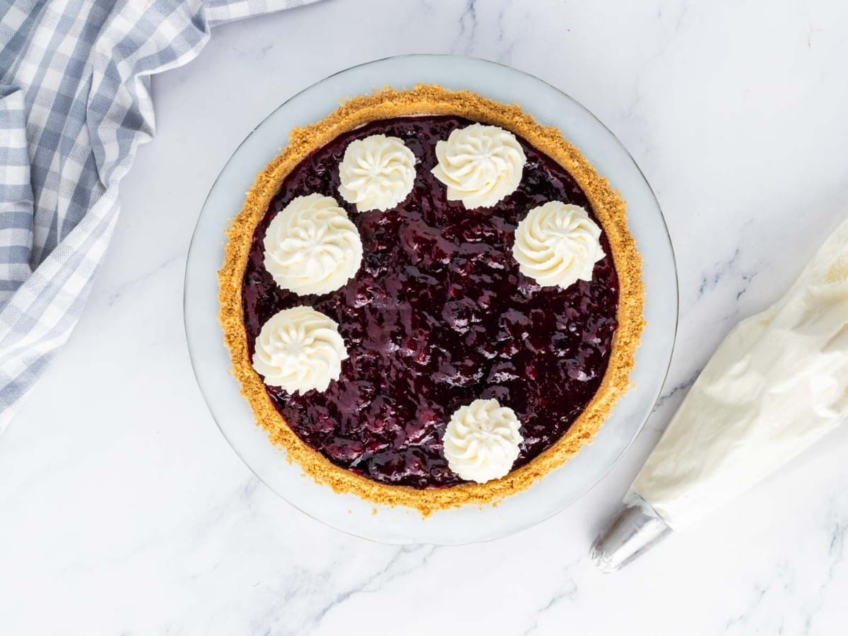 Piping whipped cream on top of pie with a piping bag.