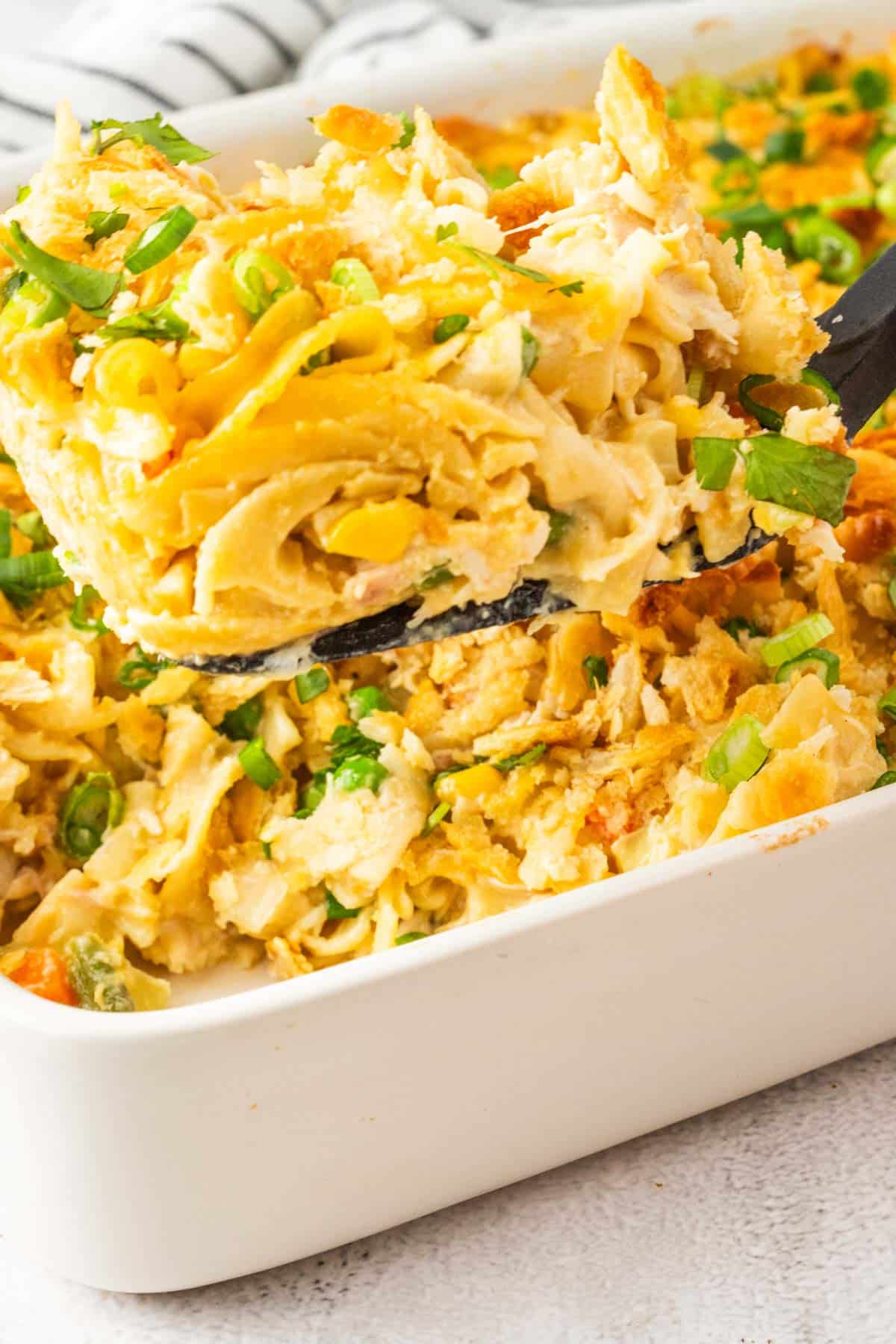 Removing a scoop of chicken casseroles with noodles from a baking dish with a spatula.