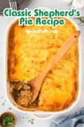 Classic Shepherd's pie in a white casserole dish with a wooden spoon sitting the the casserole where a scoop was removed.