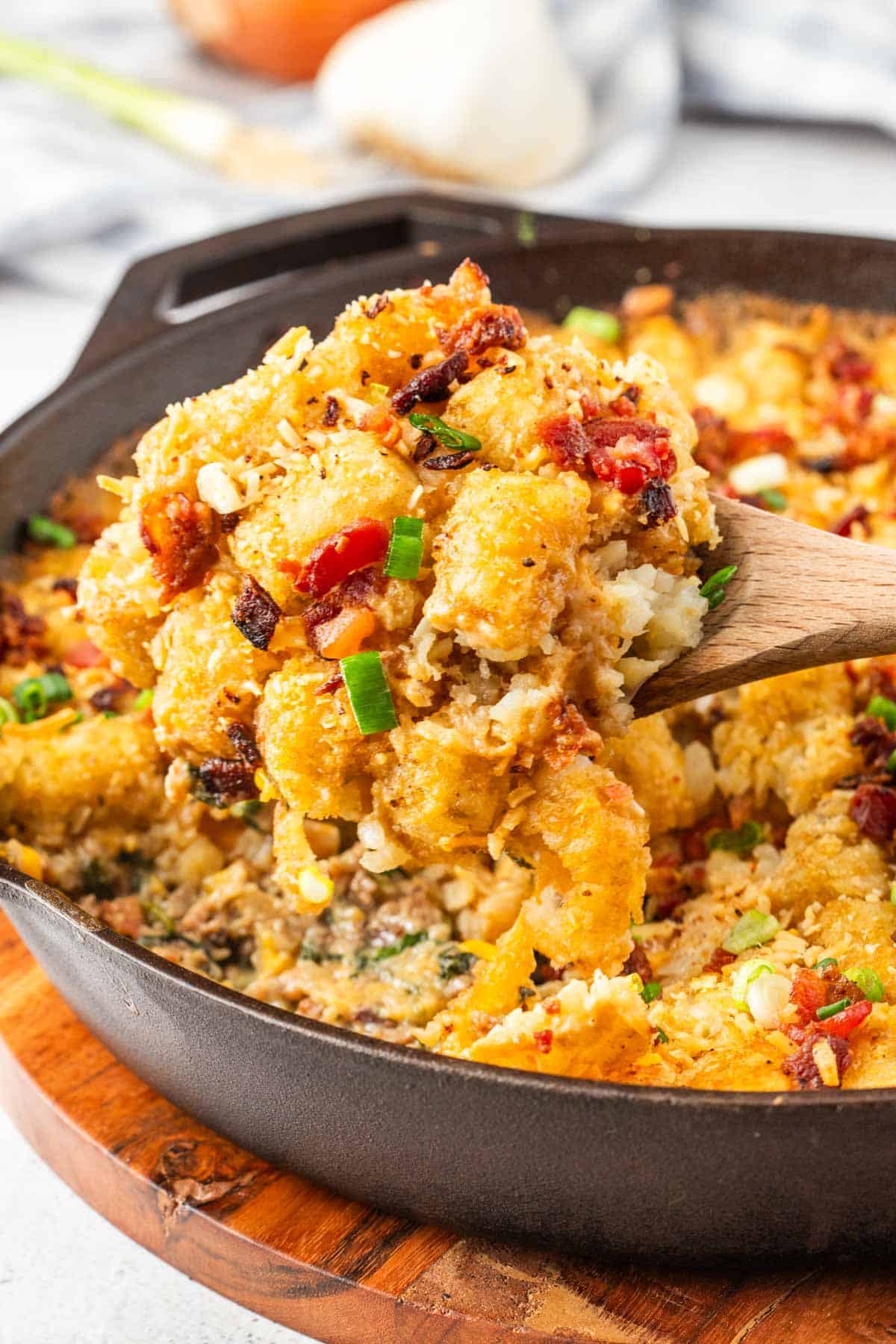 Removing a scoop of cowboy tater tot casserole from the skillet with a wooden spoon.