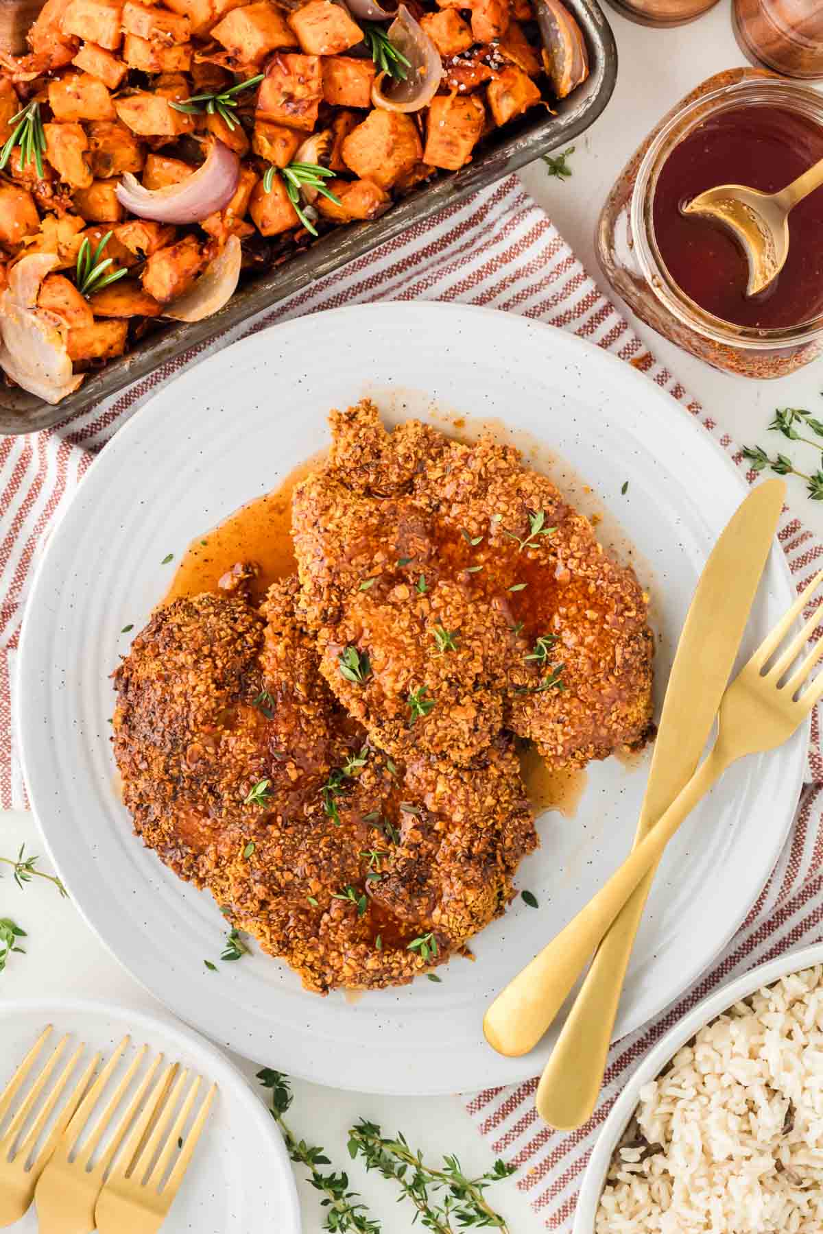 Two hot honey chicken cutlets on a white plate with a gold fork and knife.