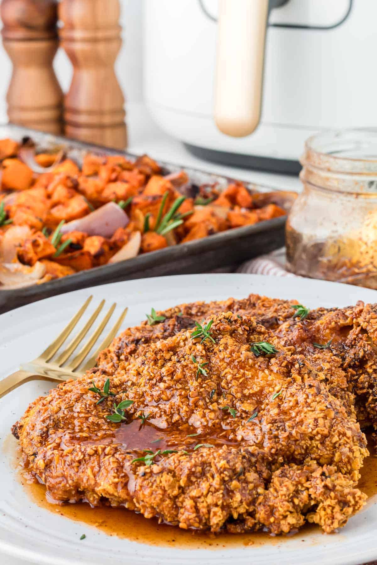 Hot honey chicken on a white plate with a pan of vegetables in the background.