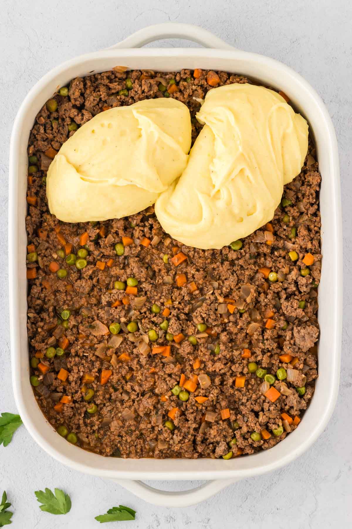 A casserole dish filled with ground beef filling and then adding mashed potatoes to the top.