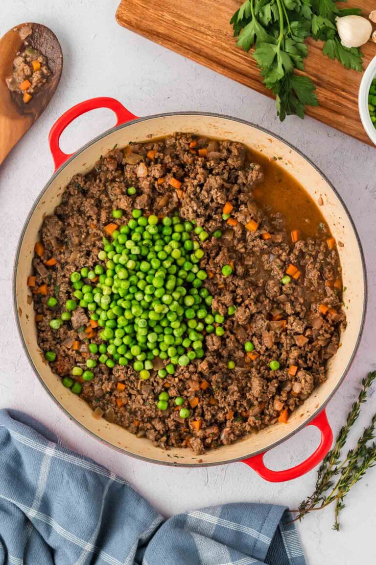 Ground beef mixture for shepherd's pie in a pot with green peas and beef broth added.