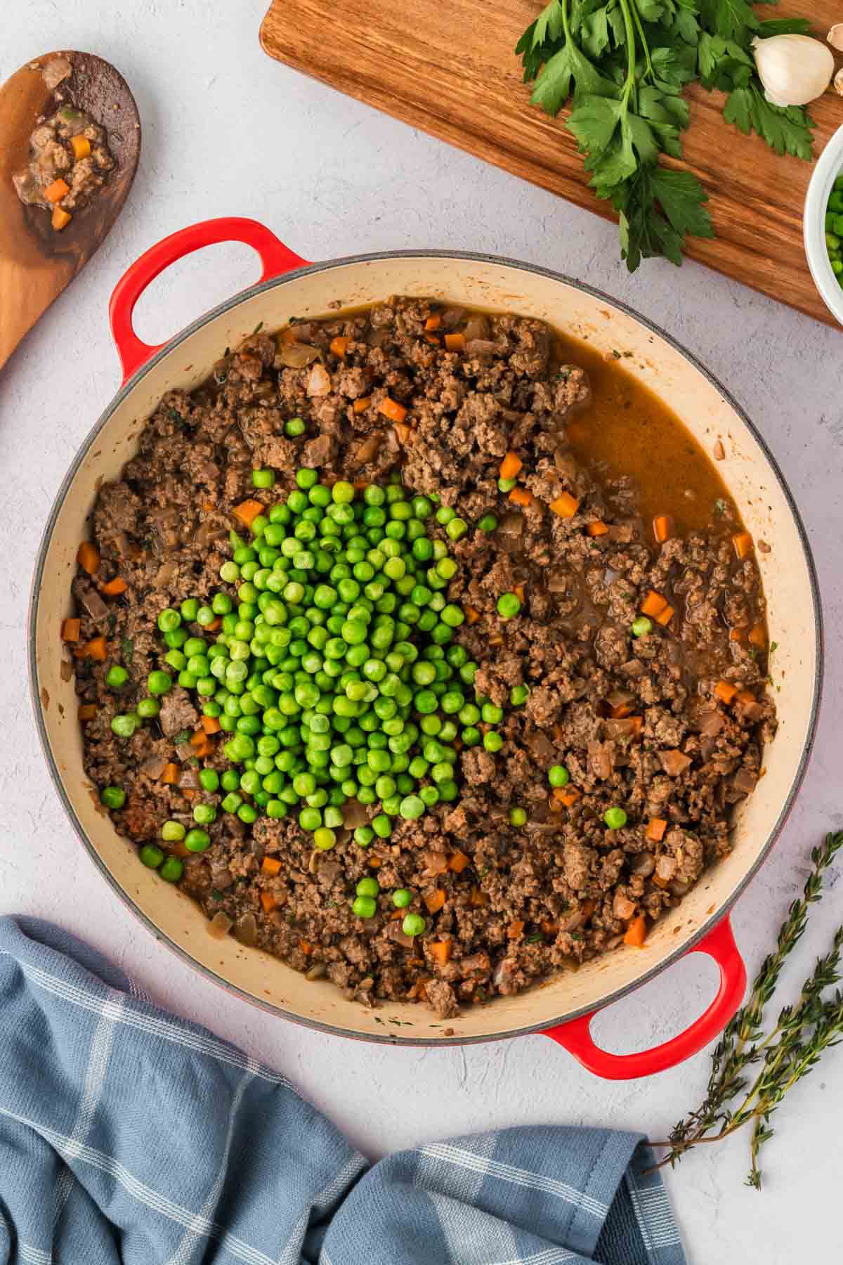 Ground beef mixture for shepherd's pie in a pot with green peas and beef broth added.