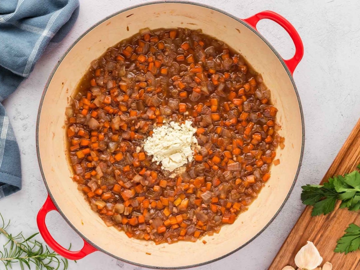 A pot with caramelized onions and carrots deglazed with wine and a spoon of flour added to the top.