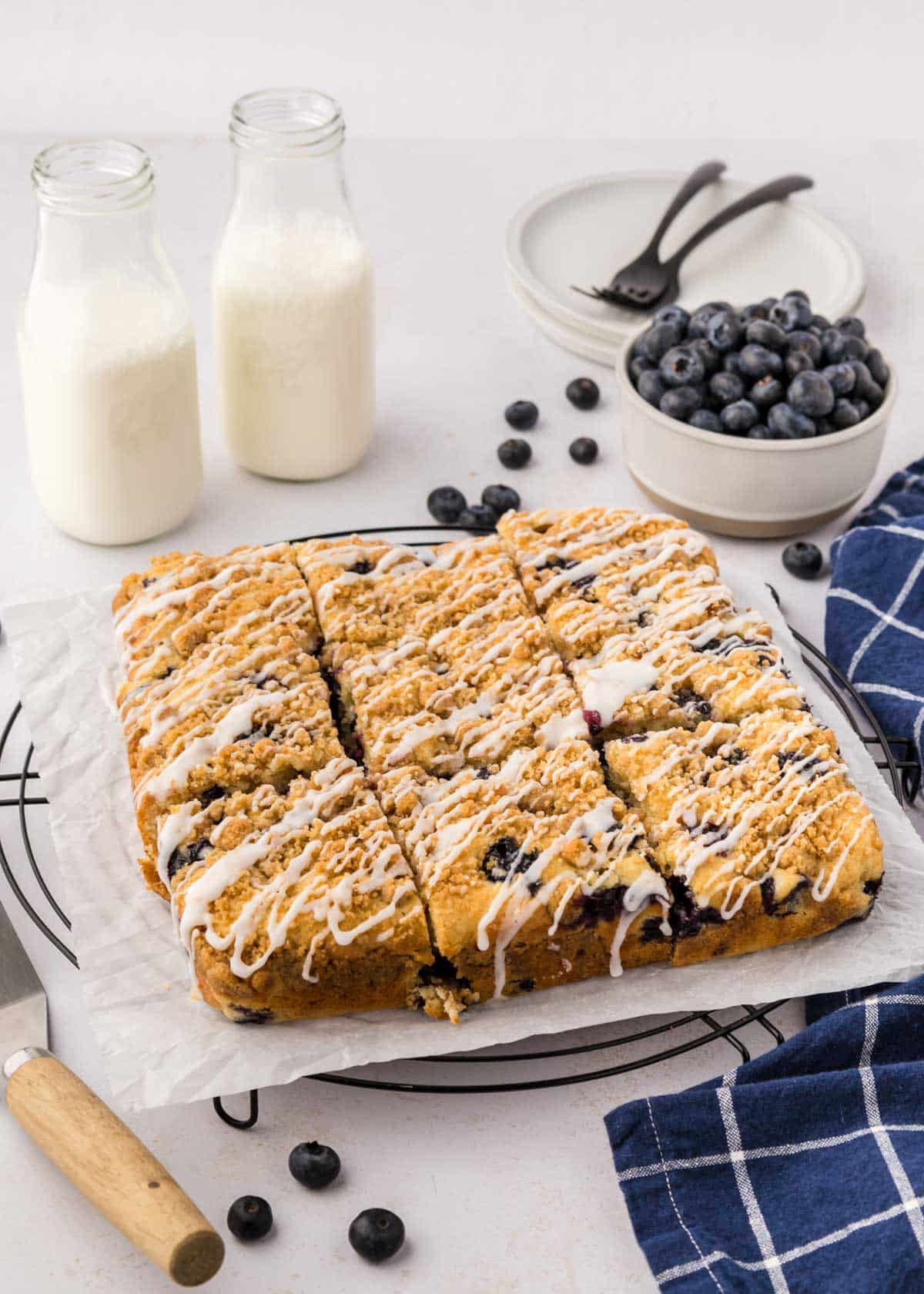 A blueberry coffee cake on a round cooling rack with a wooden serving spatula.