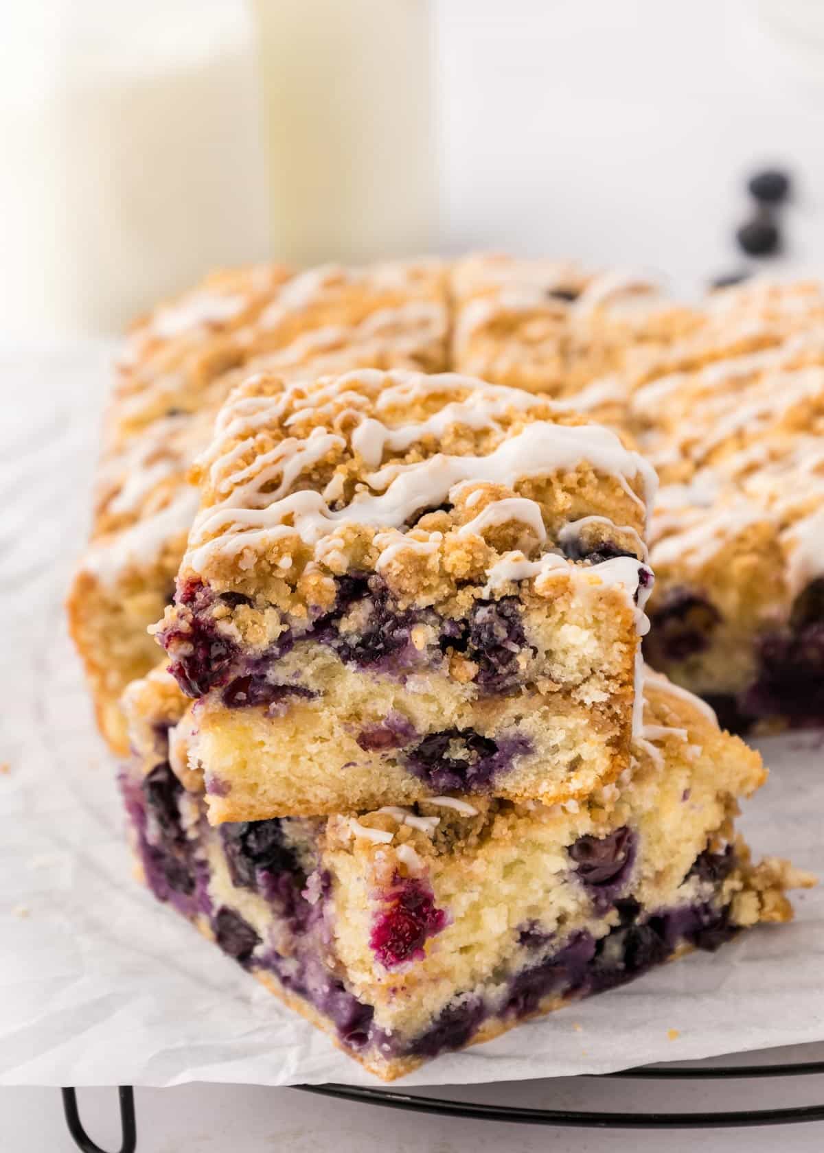 Two slices of blueberry sour cream coffee cake stacked on top of each other with the rest of the cake in the background.
