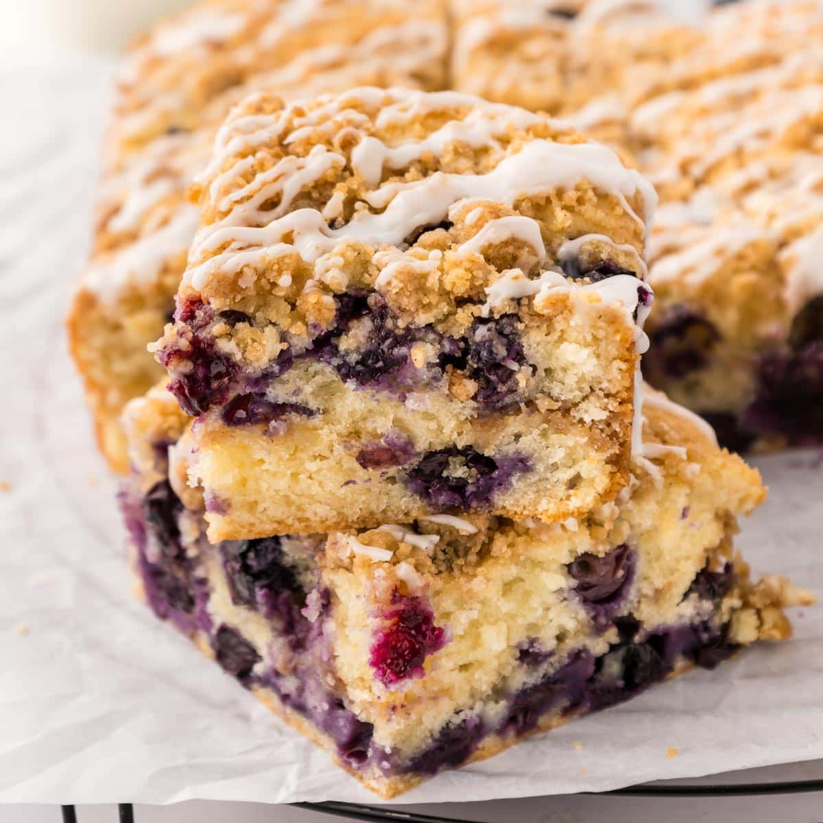 Two slices of blueberry coffee cake stacked on top of each other with the rest of the cake in the background.