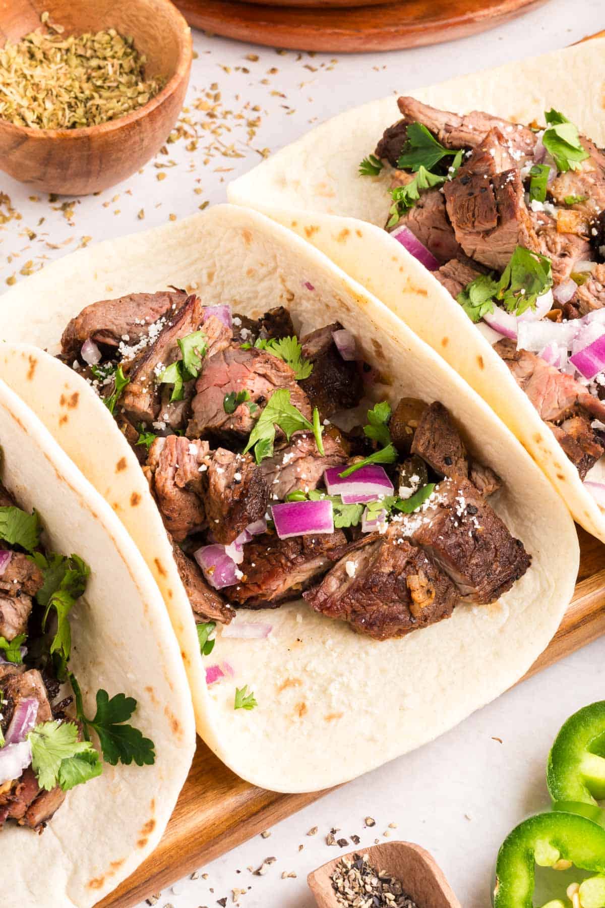 Three steak tacos on a cutting board.