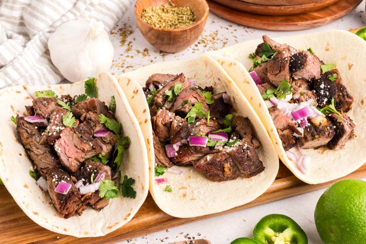 Three carne asada tacos topped with onions and cilantro.