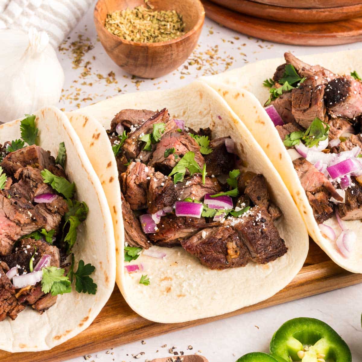 Three carne asada tacos topped with onions and cilantro.